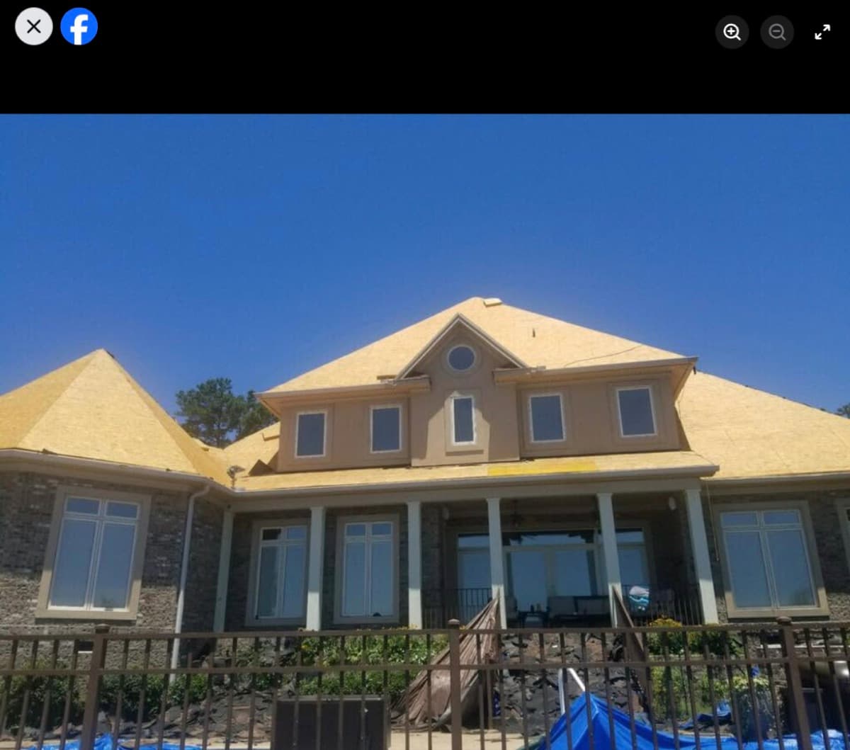 Roof installation in progress with plywood decking on a two-story home